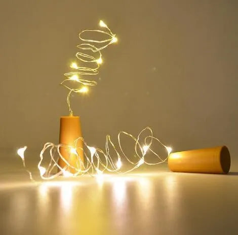 Silver wire LED string lights coiled around wine bottle with illuminated bulbs and bottle stopper fitting