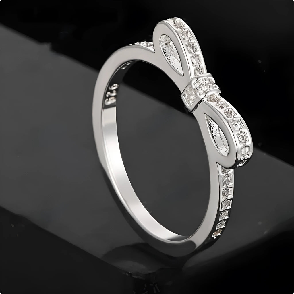 Silver-coloured bow-shaped ring with rhinestone and zircon crystal decoration on a white background.