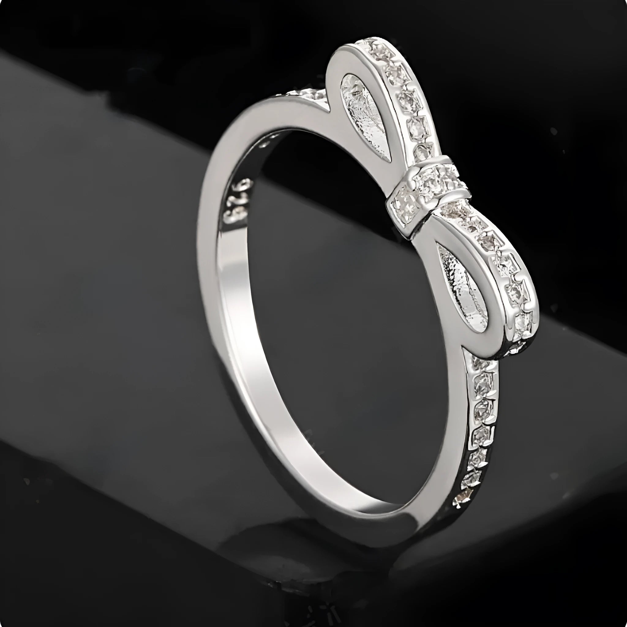 Silver-coloured bow-shaped ring with rhinestone and zircon crystal decoration on a white background.