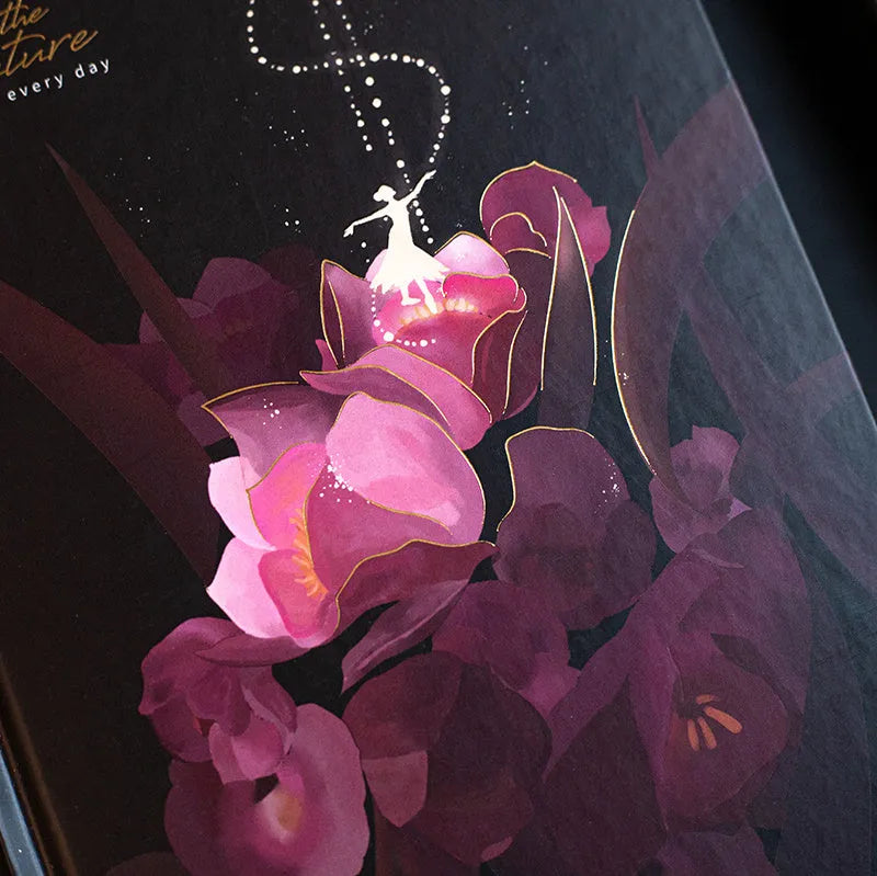 A5 notebook with a luminous cover open to show pages with colour illustrations, in deep blue, gold, light blue, or purple.
