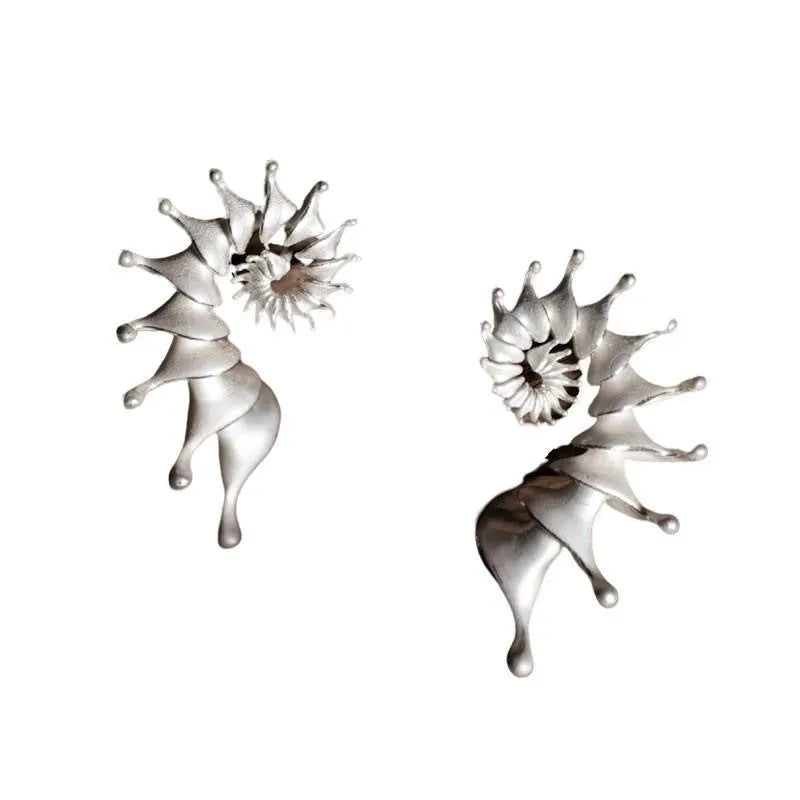 A pair of three-dimensional conch-shaped ear studs with a matte metallic finish.
