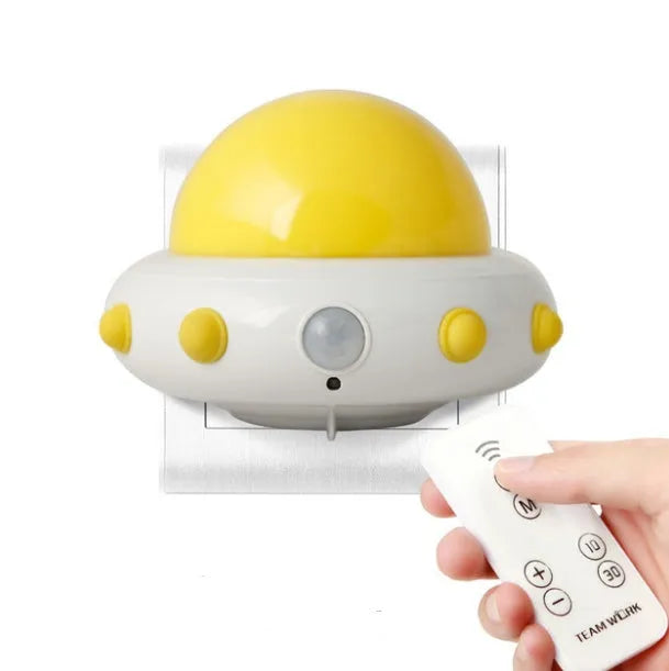 A small blue UFO-shaped bedside night light with a remote control on a wooden table.