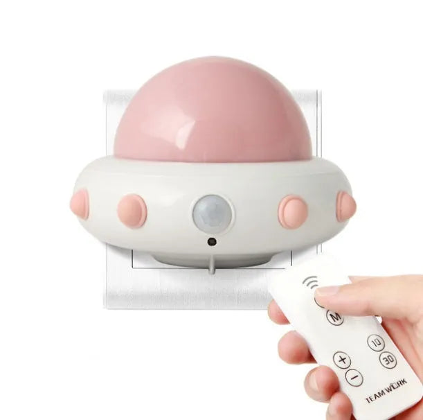 A small blue UFO-shaped bedside night light with a remote control on a wooden table.