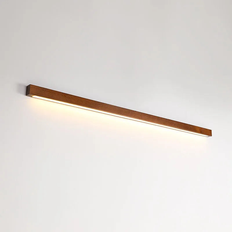 Walnut coloured log strip wall lamp with a square wood and acrylic profile mounted on a wall.