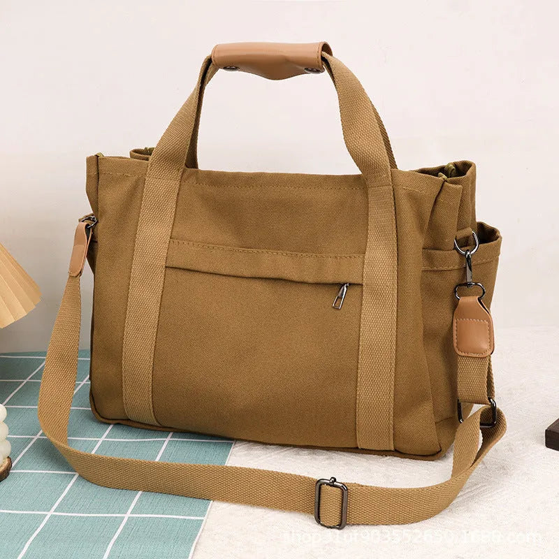 Large horizontal square canvas tote bag with cross-body strap, shown in army green colour with visible sewing lines.