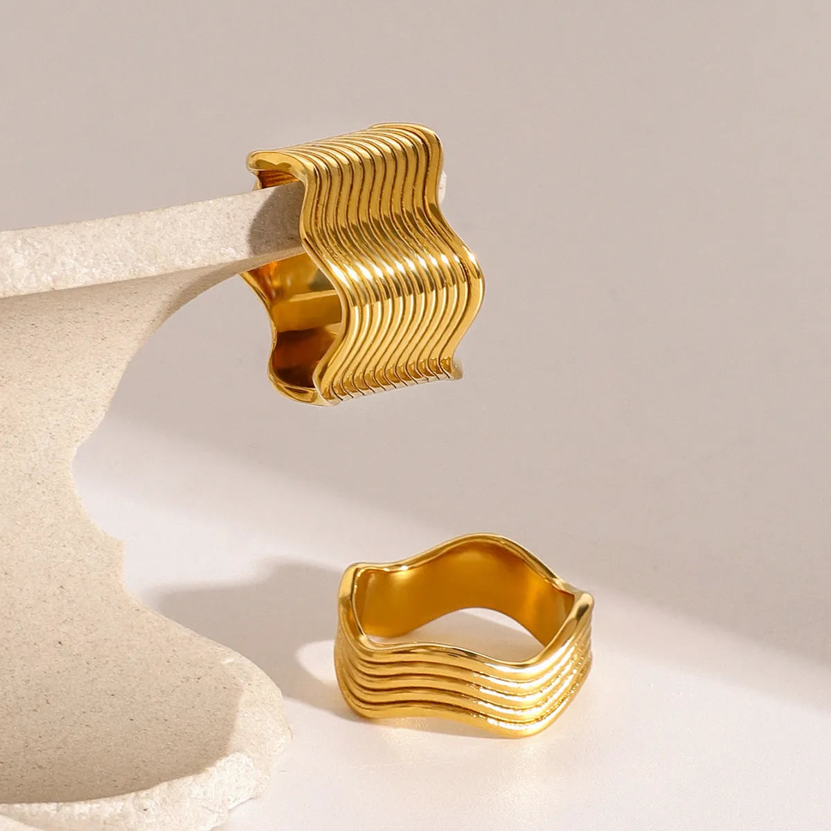 A women's stainless steel ring with a wide, sculptural geometric wave design and an electroplated silver-toned finish.