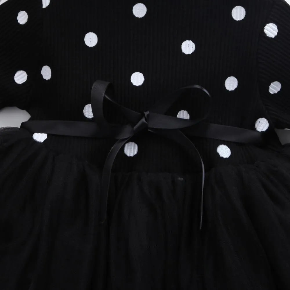 A baby girl wearing a long sleeve black tutu and lace dress for a birthday party.