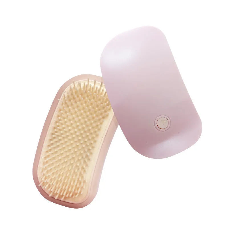 Handheld pink and white electric pet massage brush for cats and dogs on a table.
