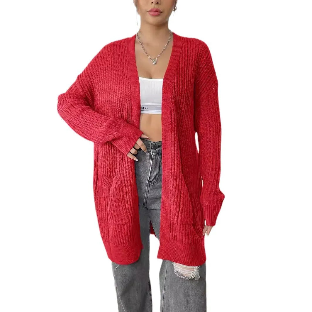 A woman wearing a loose-fitting, mid-length dark green cardigan sweater with double pockets.