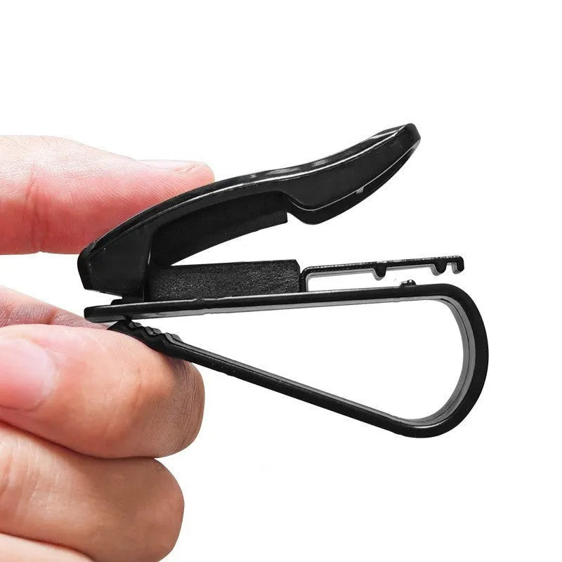 Black plastic clip for car sun visor holding a pair of glasses and a ticket.