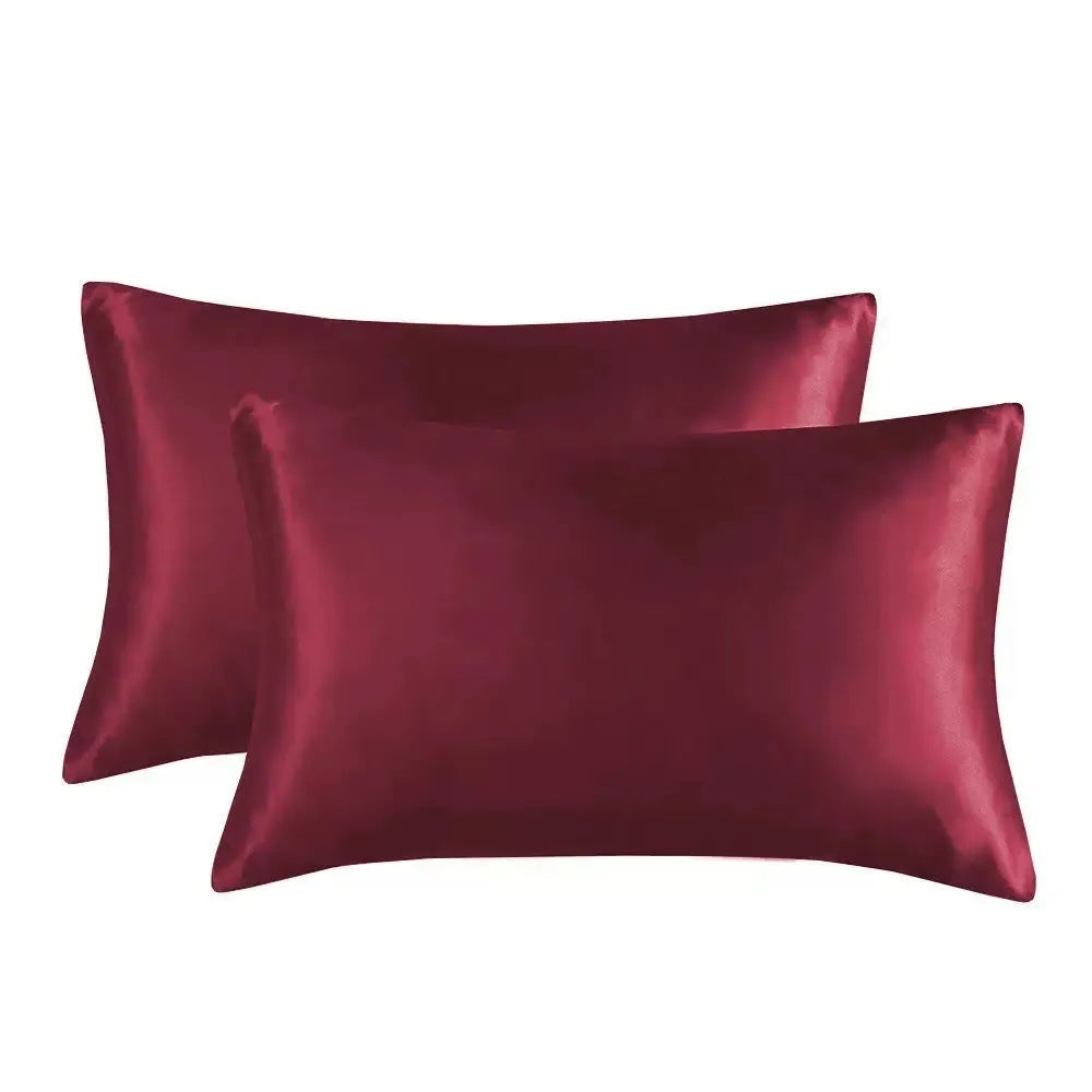 Pair of solid colour satin pillowcases in polyester fabric on a bed.