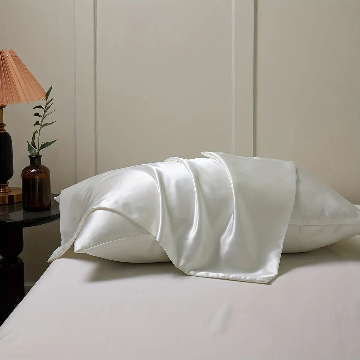 Pair of solid colour satin pillowcases in polyester fabric on a bed.