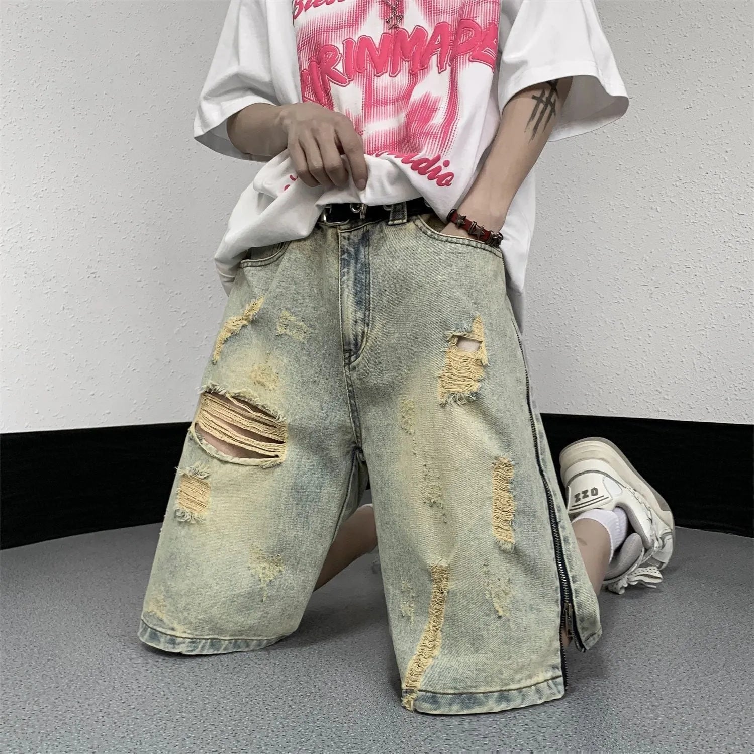 Men's blue denim shorts with yellow mud wash effect, ripping details, button fly, and loose straight-leg fit