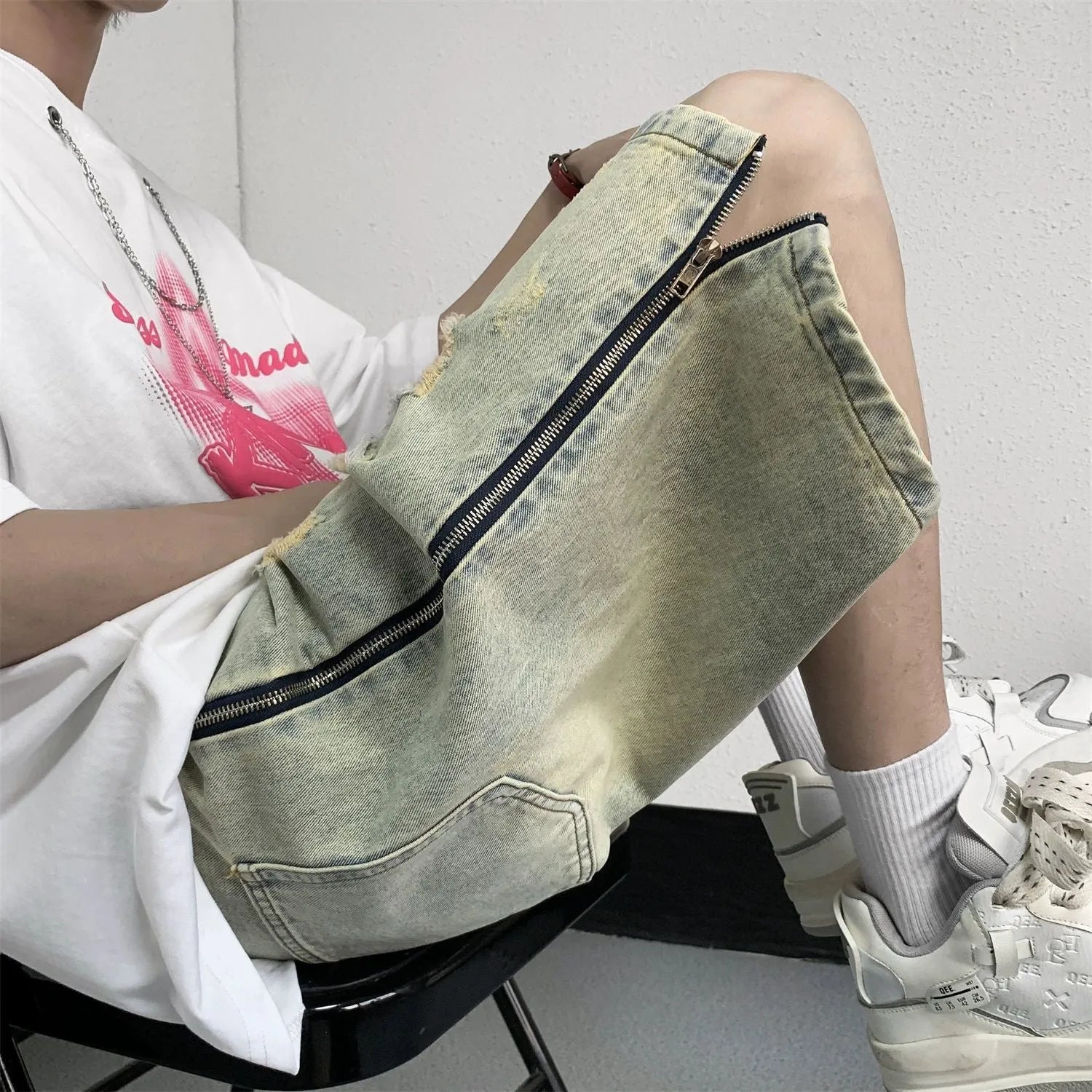 Men's blue denim shorts with yellow mud wash effect, ripping details, button fly, and loose straight-leg fit