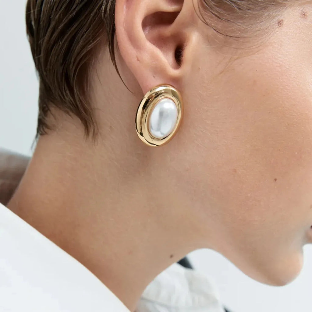 A pair of stainless steel stud earrings for women featuring a single vintage pearl, with butterfly clutch backings visible.