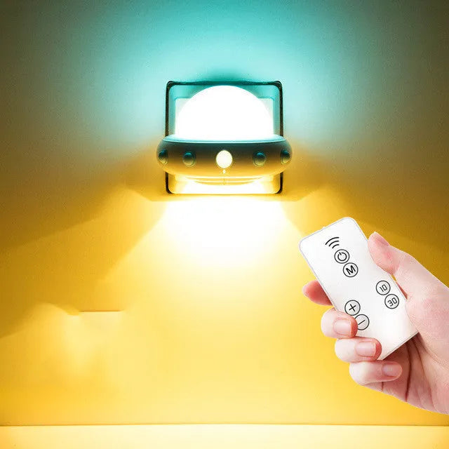 A small blue UFO-shaped bedside night light with a remote control on a wooden table.