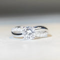 Silver moissanite ring with twisted arm band and four-claw setting holding 1 karat stone