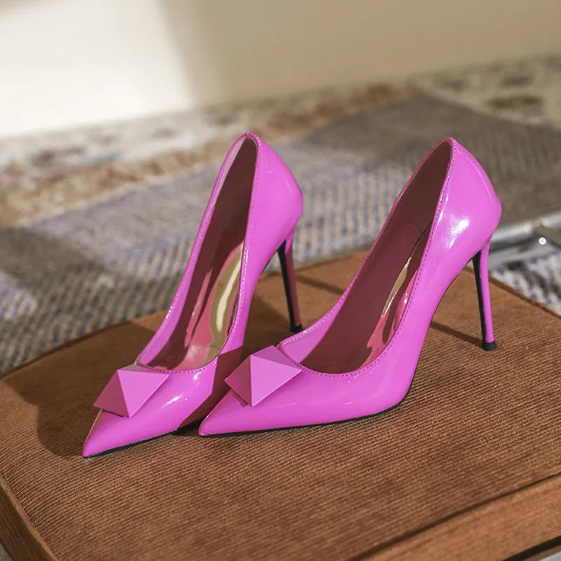 Pink women's pointed toe stiletto high heels with patent leather upper, rivet buckle detail, and a tall thin heel.