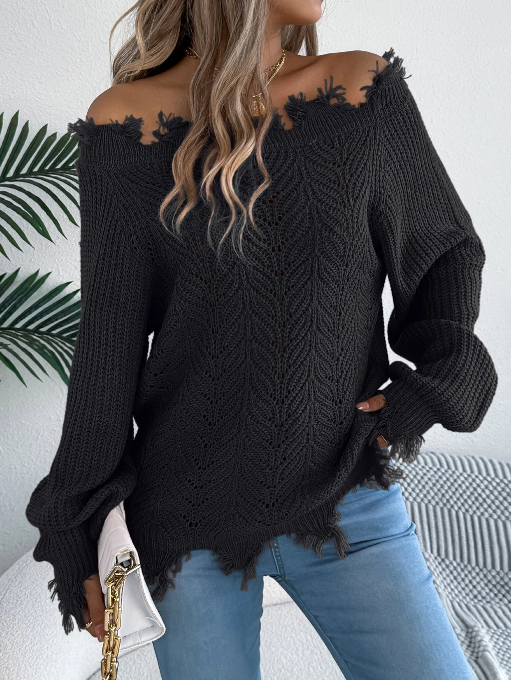 A woman wearing a white hollow-out cut off-the-shoulder pullover sweater in a street fashion style.