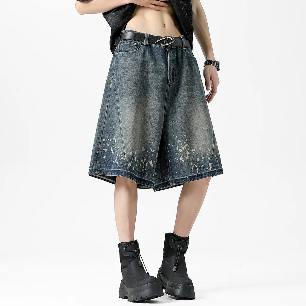 Man wearing retro blue denim shorts with ripped and splash-ink distressing on a straight-leg cut.