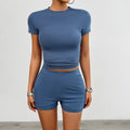 Women's solid colour two-piece sports set with round neck t-shirt and elastic shorts.