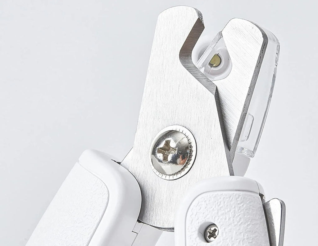 White pet nail clippers with LED light, open transparent splash guard, and separate nail file on a table