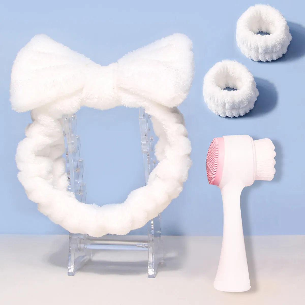 Keep dry facial brush set with plastic handle, coral fleece hair band, and stack of purple and pink face wash sponge suits.