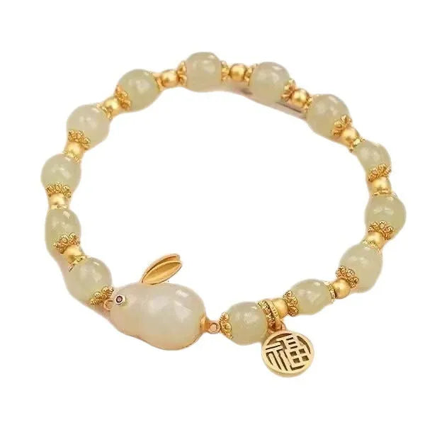 Close-up of a women's black adjustable bracelet with a green jade hare charm, fu character, and lily motif.