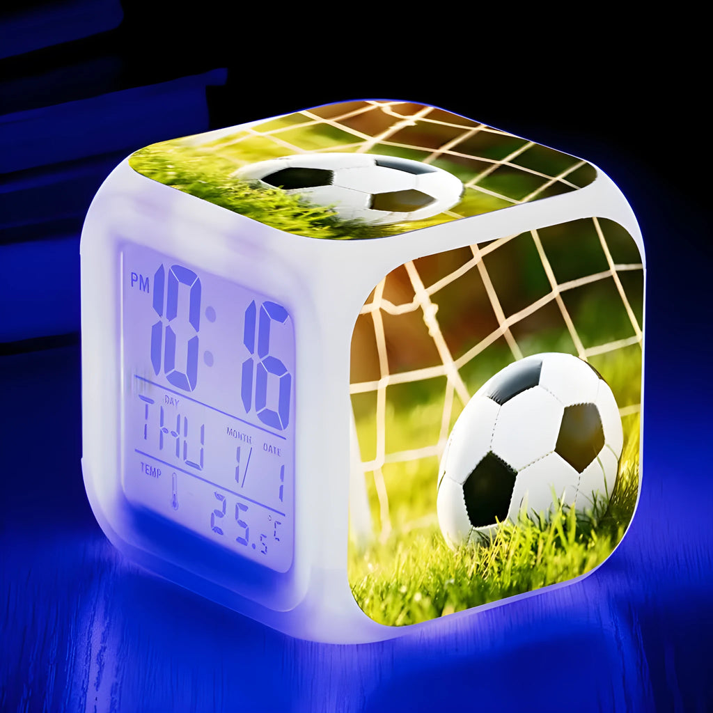 Square football-themed children's alarm clock with mute function on a desk.