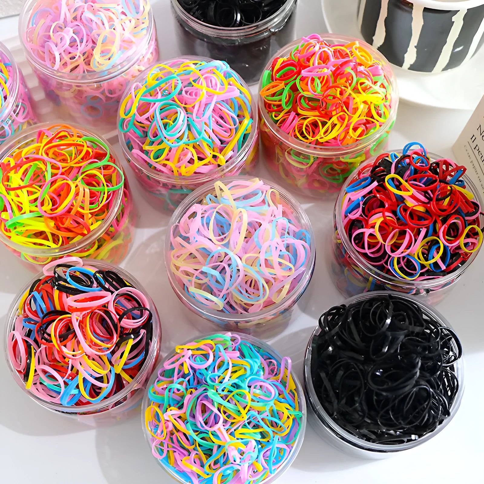 Assortment of colourful thin TPU baby hair ties in a clear reusable plastic container.