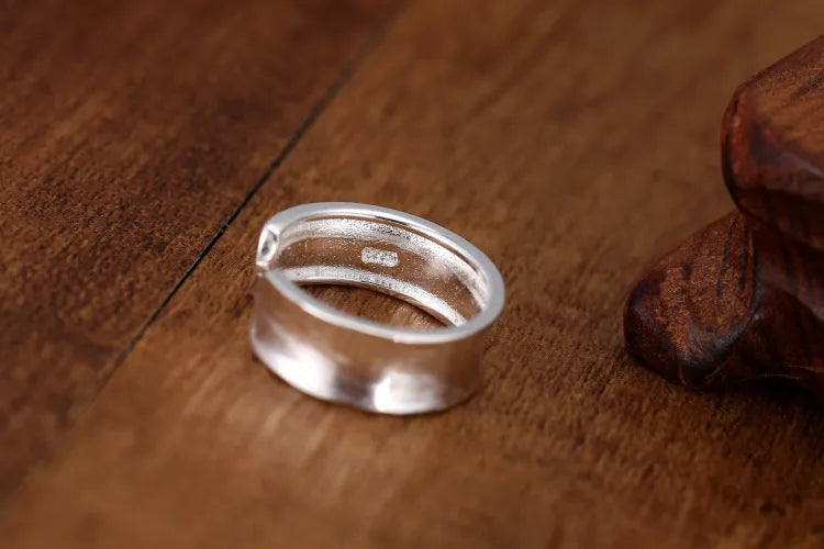 Adjustable open ring in frosted sterling silver with a geometric shape on a grey background.