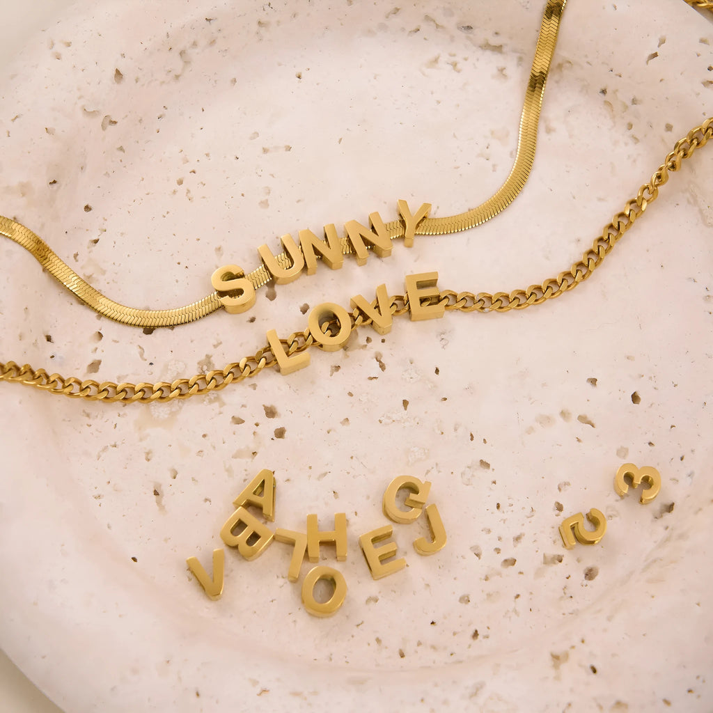 Gold and silver titanium steel necklaces showing letter A and number 7 pendants on 40.5cm chains.