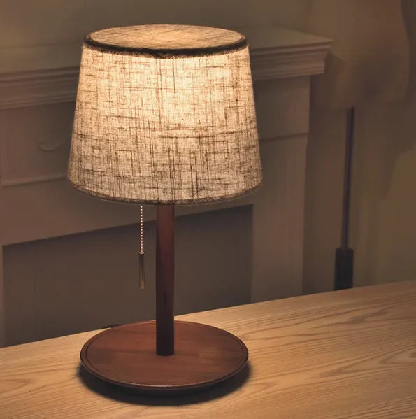 Walnut coloured solid wood desk lamp with a white fabric lampshade and a cable switch.