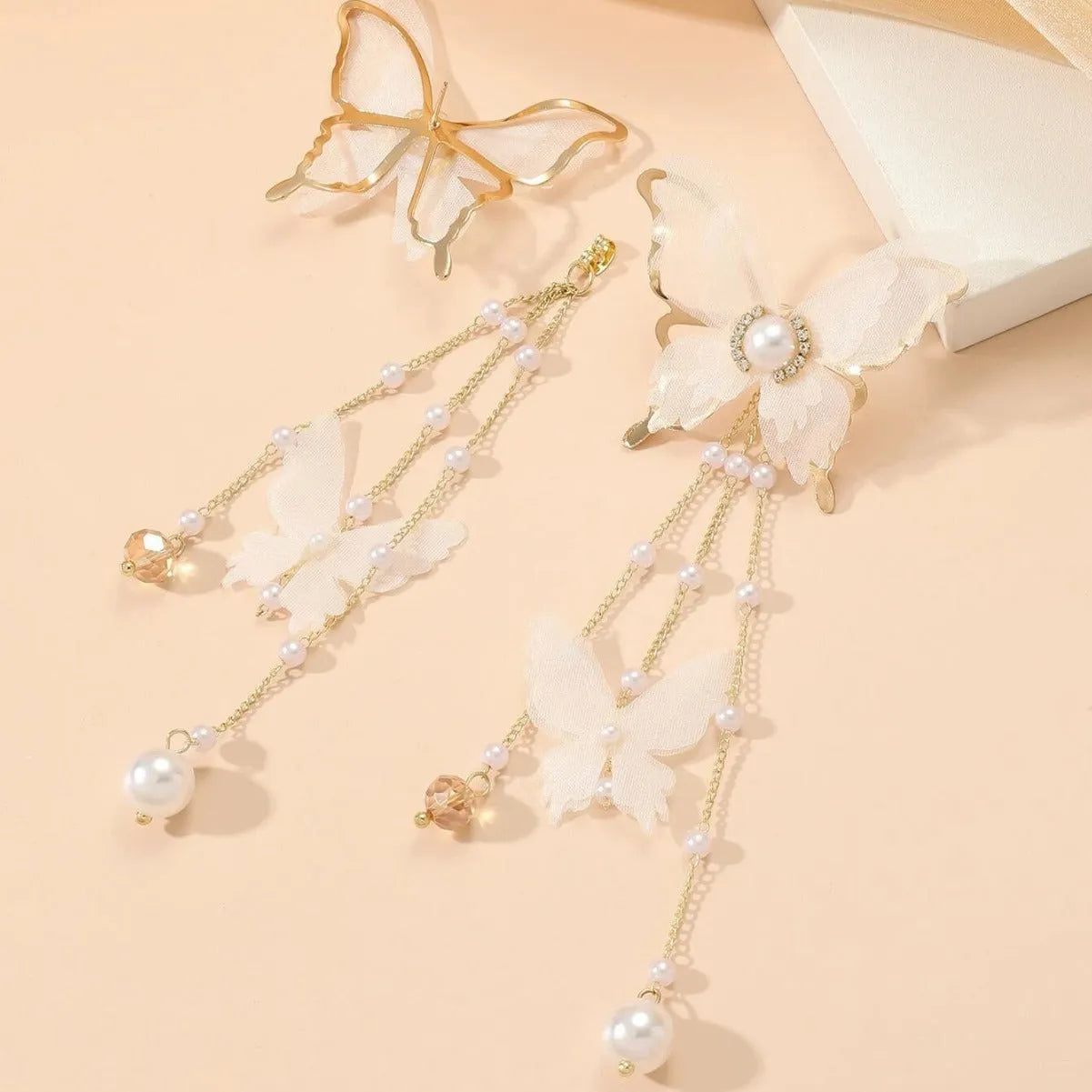 Close-up of a white butterfly-shaped earring with lace detail, pearls, rhinestones, and a long tassel.