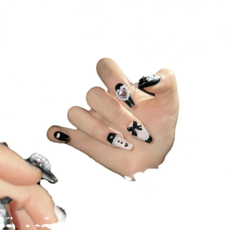 Black and pink heart-shaped press-on false nails with bow design, shown in mid-length cat's eye style.