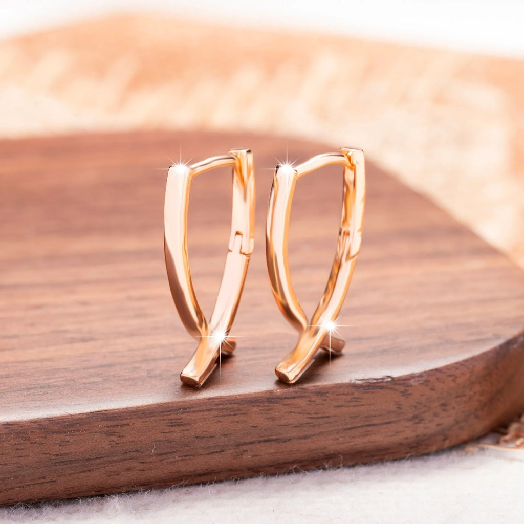 A pair of rose gold coloured cross-shaped earrings on a white background.