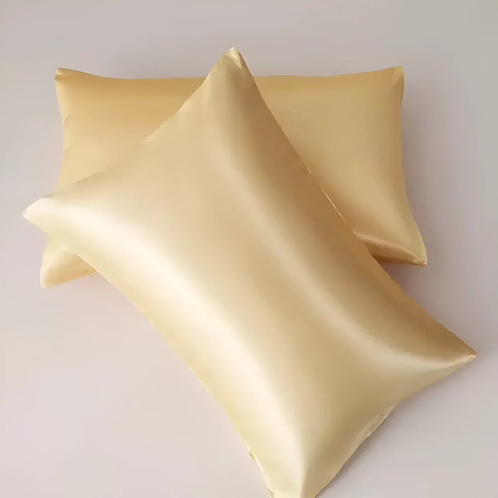 Pair of solid colour satin pillowcases in polyester fabric on a bed.