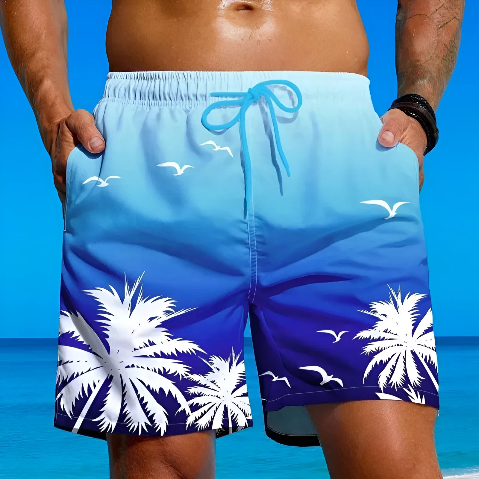 Man wearing loose blue board shorts-style swimming trunks on a beach.