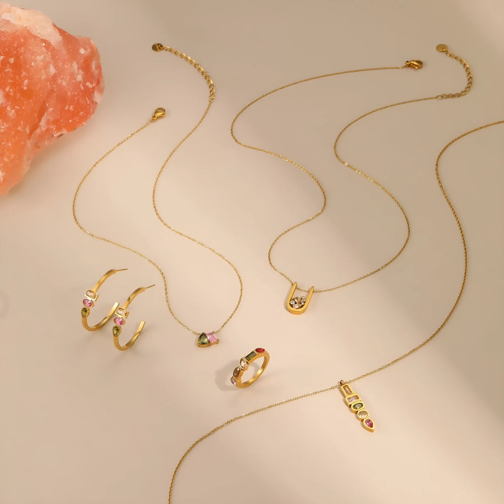 Geometric gold-plated necklace, ring, and earrings set with an adjustable chain on a grey background.
