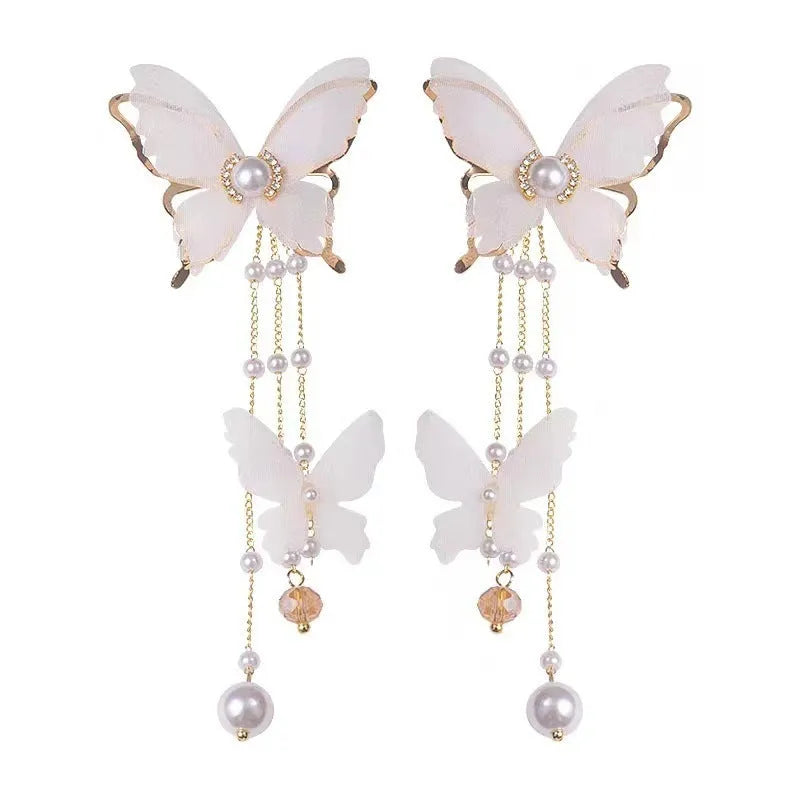 Close-up of a white butterfly-shaped earring with lace detail, pearls, rhinestones, and a long tassel.