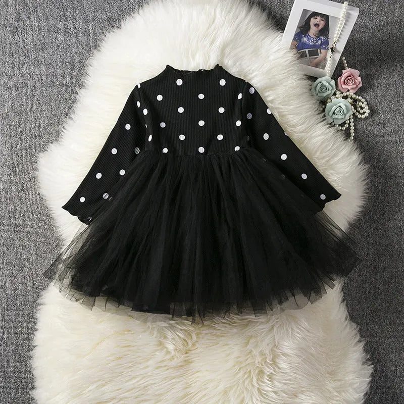 A baby girl wearing a long sleeve black tutu and lace dress for a birthday party.