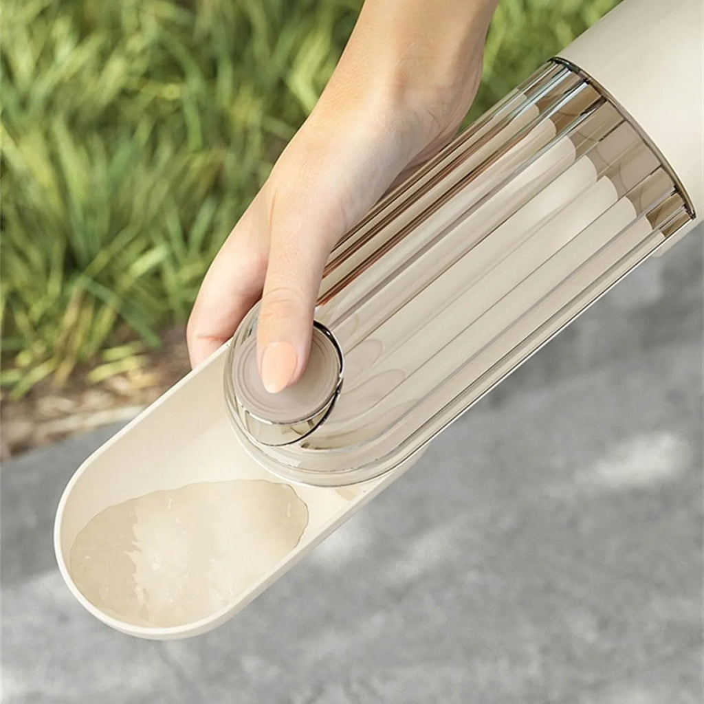 Beige foldable dog water bottle and food dispenser with tray, shown next to a dog on a walk.