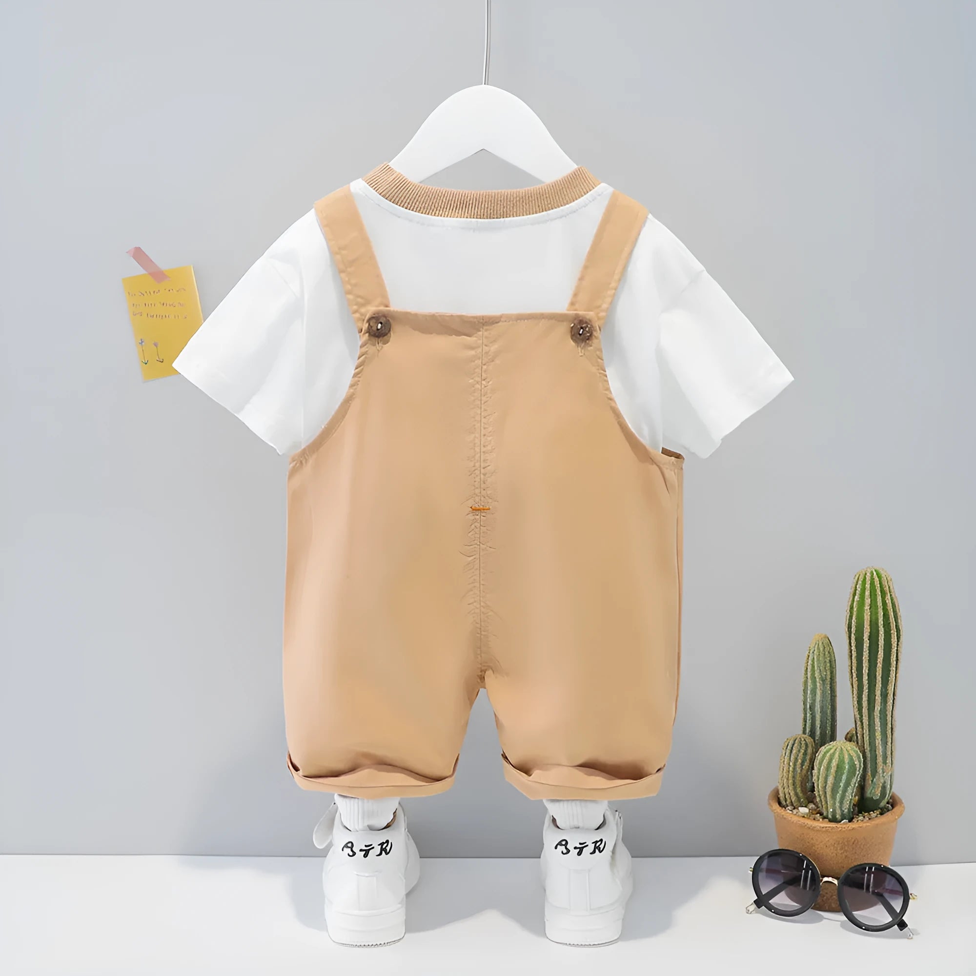 Yellow cotton baby romper with cartoon print and openable shoulder straps, laid flat.