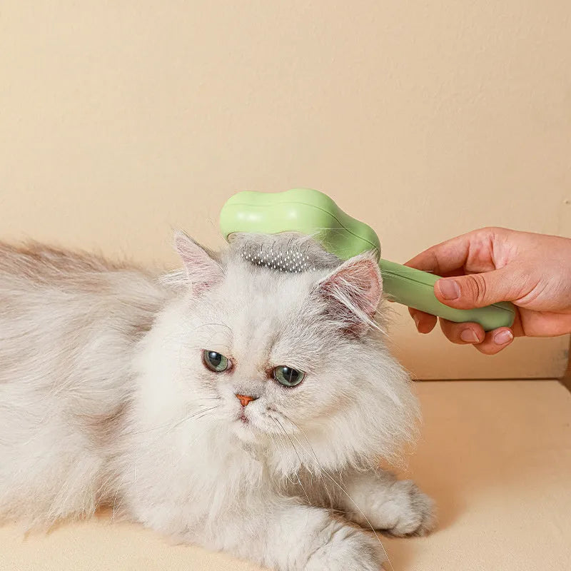 Green stainless steel self-cleaning cat comb with needle bristles on a white background.