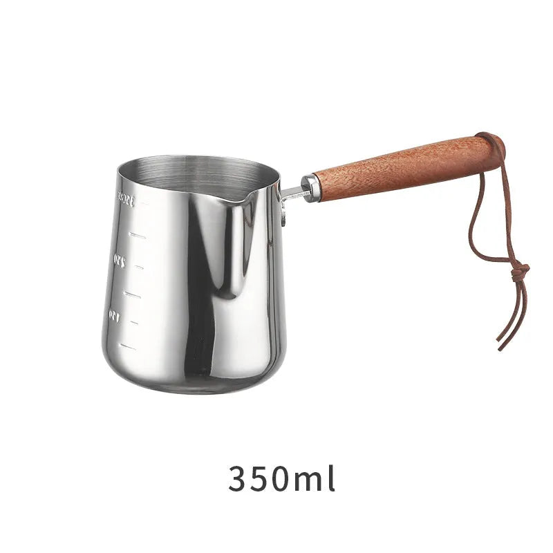 Stainless steel coffee mug with measurement scale and a light wood handle on a wooden table.