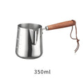 Stainless steel coffee mug with measurement scale and a light wood handle on a wooden table.
