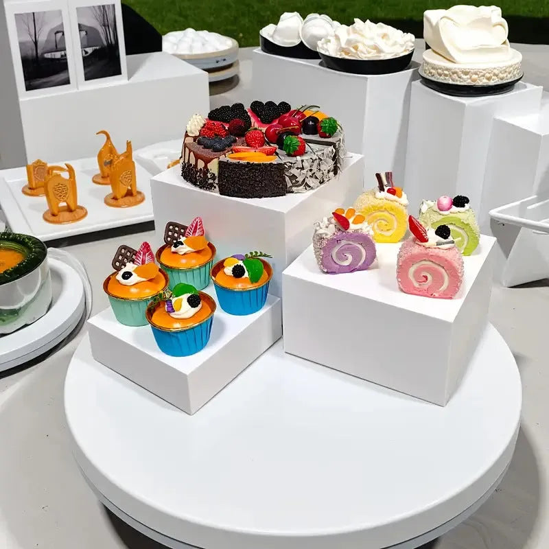 White plastic dessert table display stand with six cube-shaped racks for cakes and pastries.