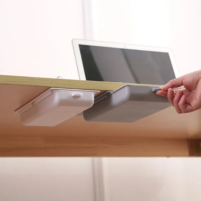 Adhesive under table storage drawer in plastic with covered grid design, shown in grey colour