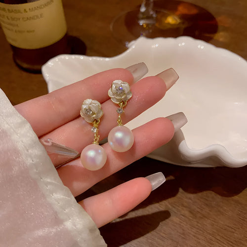 Close-up of a pair of pearl-finished camellia flower stud earrings made from alloy metal.