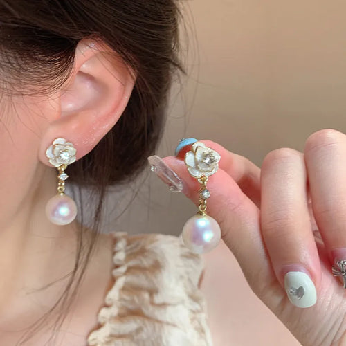 Close-up of a pair of pearl-finished camellia flower stud earrings made from alloy metal.